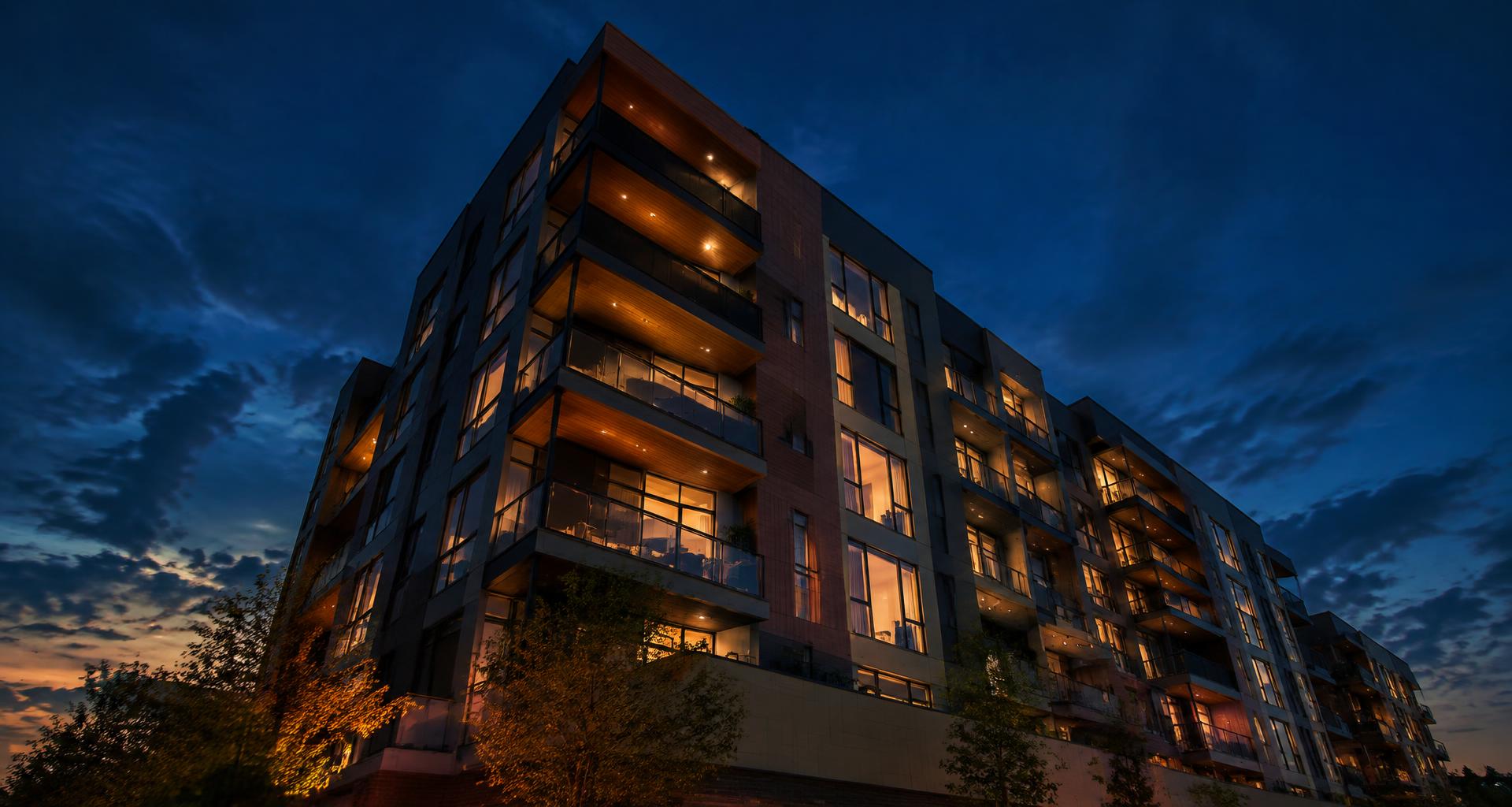 A modern residential building glowing warmly at dusk